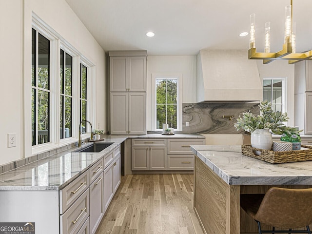 kitchen with light hardwood / wood-style floors, sink, light stone countertops, and custom range hood