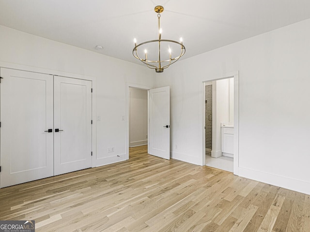 unfurnished bedroom featuring a notable chandelier, light hardwood / wood-style floors, a closet, and ensuite bathroom