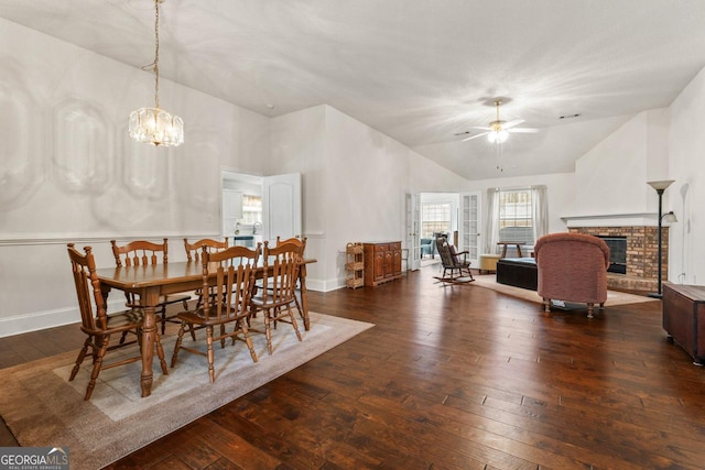 dining space featuring dark hardwood / wood-style flooring, a brick fireplace, ceiling fan with notable chandelier, and high vaulted ceiling