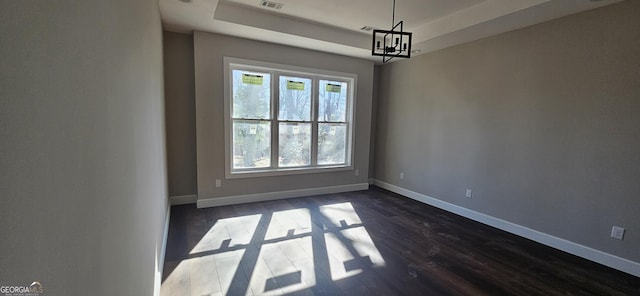 unfurnished room featuring a notable chandelier, dark wood-type flooring, and a raised ceiling