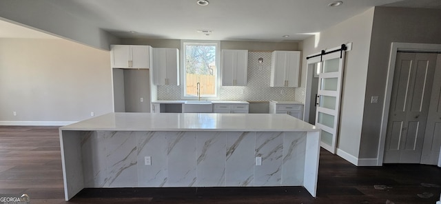 kitchen with a kitchen island, a barn door, white cabinets, and backsplash