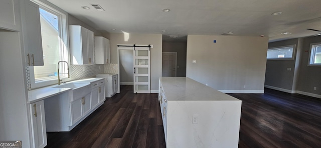 kitchen with sink, white cabinetry, tasteful backsplash, dark hardwood / wood-style flooring, and a barn door