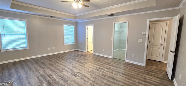 unfurnished bedroom featuring ornamental molding, a tray ceiling, dark hardwood / wood-style flooring, and a spacious closet