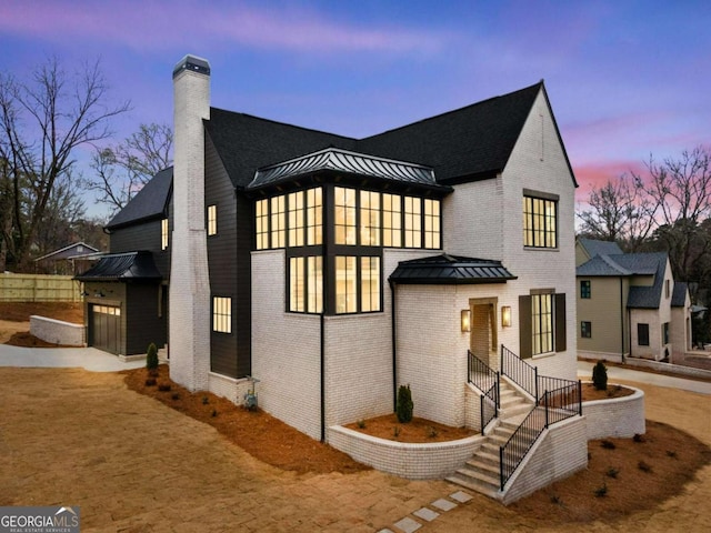 view of front of property featuring a standing seam roof, concrete driveway, brick siding, and a chimney