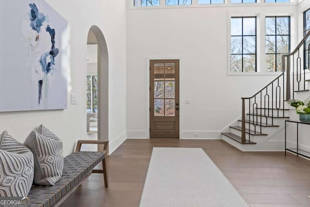 foyer with arched walkways, plenty of natural light, stairway, and wood finished floors