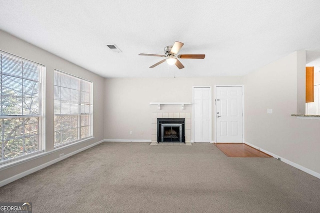 unfurnished living room with a tiled fireplace, carpet floors, a textured ceiling, and ceiling fan