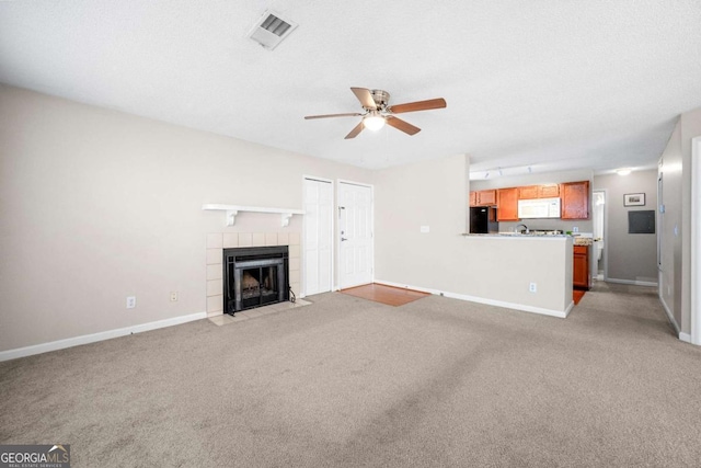 unfurnished living room featuring a tiled fireplace, light carpet, a textured ceiling, and ceiling fan