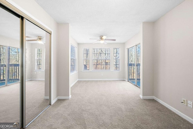 unfurnished room featuring ceiling fan, light colored carpet, a textured ceiling, and a wealth of natural light