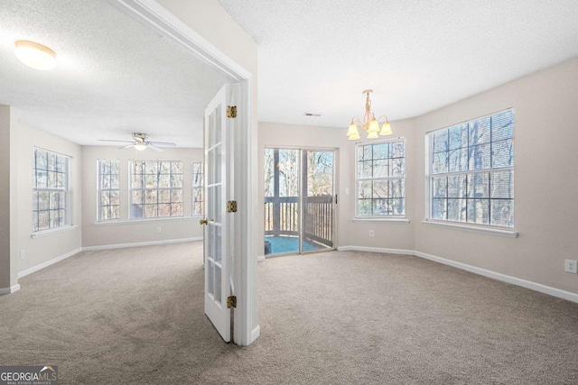 carpeted empty room featuring ceiling fan with notable chandelier, a wealth of natural light, and a textured ceiling