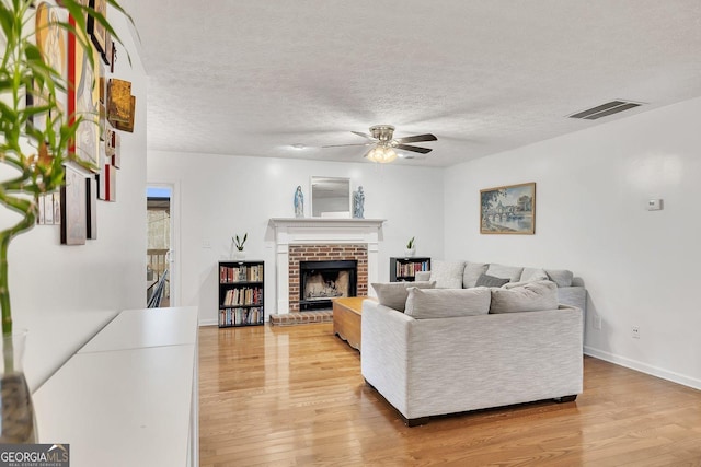 5833 Westerling Pl, Powder Springs, GA 30127 - living area featuring light wood-style floors, a ceiling fan, a brick fireplace, a textured ceiling, and baseboards