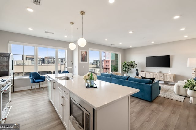 kitchen featuring pendant lighting, sink, appliances with stainless steel finishes, white cabinetry, and a kitchen island with sink