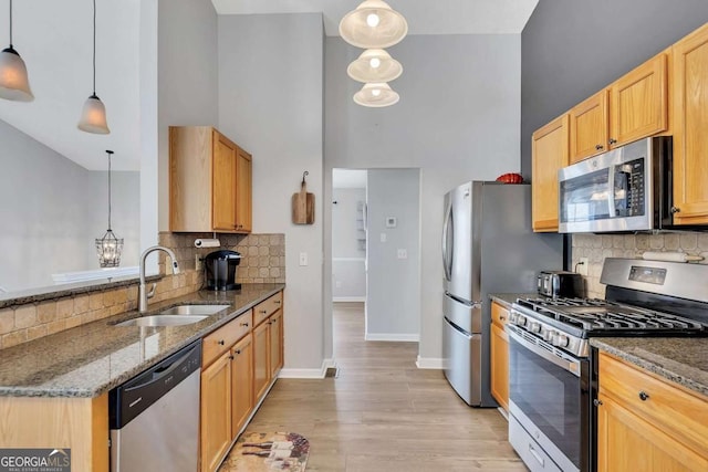 kitchen with appliances with stainless steel finishes, decorative light fixtures, sink, dark stone counters, and light hardwood / wood-style flooring