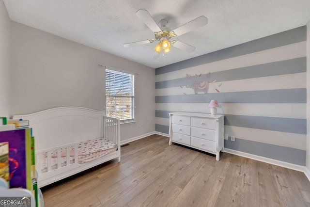 bedroom with ceiling fan, a crib, light hardwood / wood-style floors, and a textured ceiling