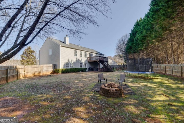 view of yard with a deck, a trampoline, and an outdoor fire pit