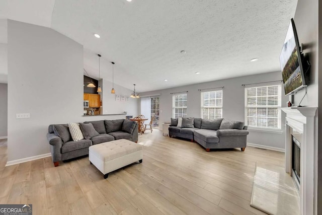 living room featuring vaulted ceiling, light hardwood / wood-style floors, and a textured ceiling