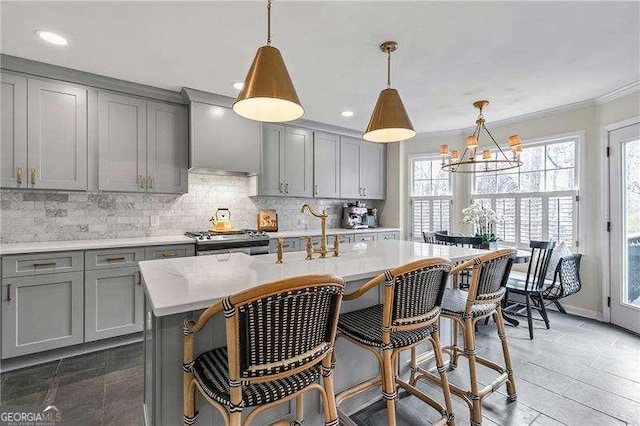 kitchen featuring a kitchen island with sink, hanging light fixtures, stainless steel range, and gray cabinetry