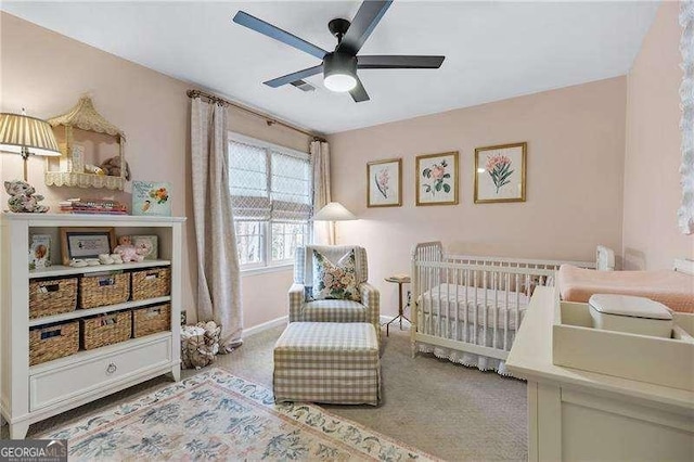 carpeted bedroom featuring ceiling fan and a crib