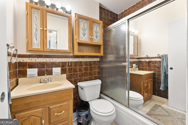 full bathroom with bath / shower combo with glass door, tile walls, vanity, and toilet