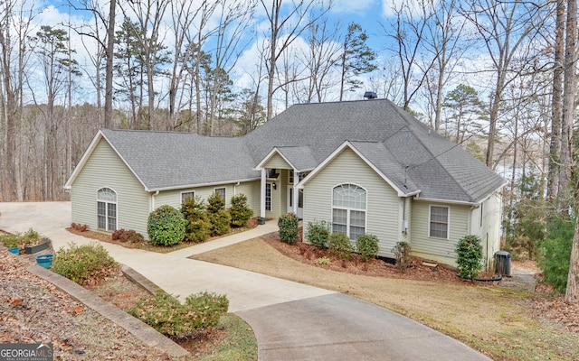 ranch-style house with concrete driveway, roof with shingles, and central AC unit