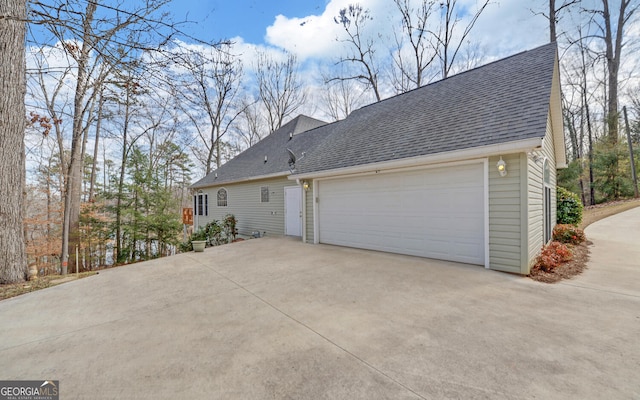 exterior space featuring driveway, an attached garage, and roof with shingles