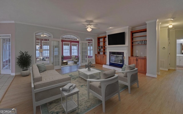 living room featuring a glass covered fireplace, visible vents, ceiling fan, and light wood-style flooring