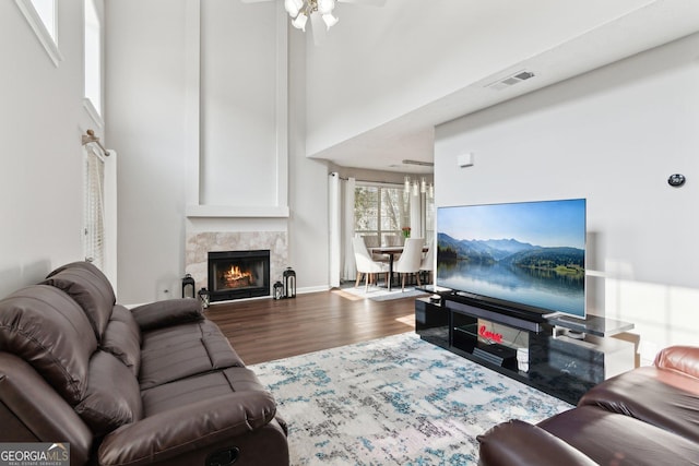 living room with a high ceiling, ceiling fan, hardwood / wood-style floors, and a high end fireplace