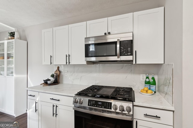 kitchen featuring light stone countertops, decorative backsplash, stainless steel appliances, and white cabinets