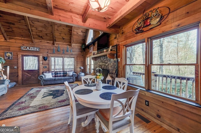 dining space featuring a stone fireplace, wood walls, vaulted ceiling with beams, hardwood / wood-style flooring, and wooden ceiling