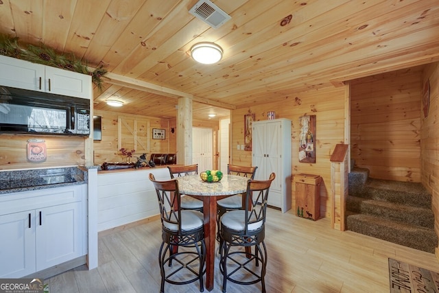 dining room with light hardwood / wood-style flooring, wooden ceiling, and wooden walls