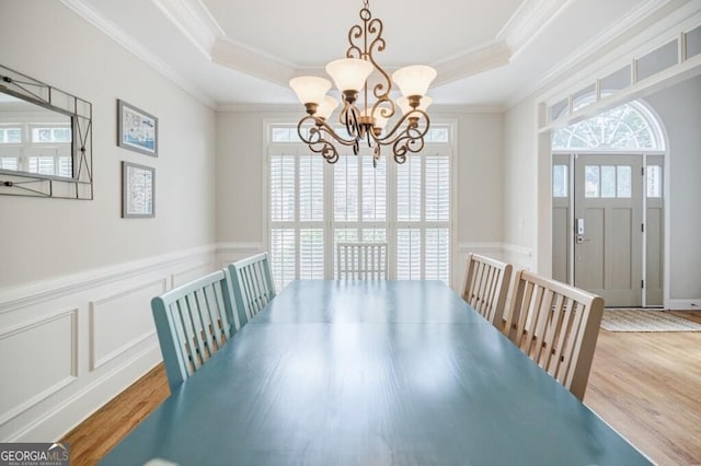 dining space featuring ornamental molding, a raised ceiling, and light hardwood / wood-style flooring