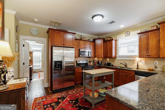 kitchen with sink, dark hardwood / wood-style flooring, dark stone counters, ornamental molding, and stainless steel appliances