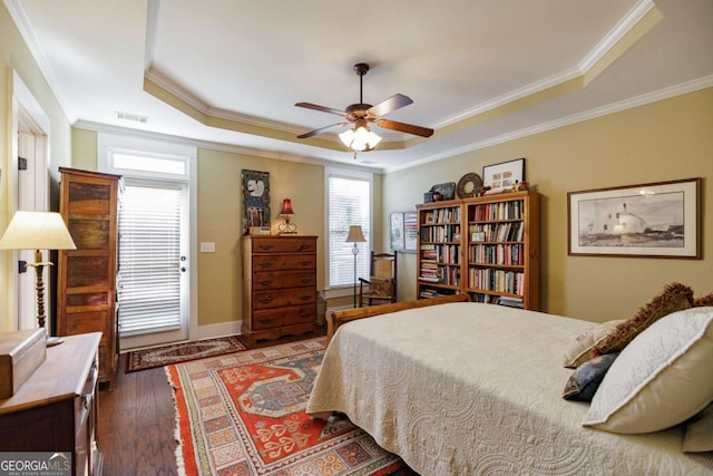 bedroom with a tray ceiling, dark wood-type flooring, ornamental molding, and ceiling fan