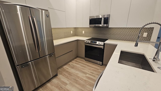 kitchen featuring sink, backsplash, white cabinets, stainless steel appliances, and light wood-type flooring