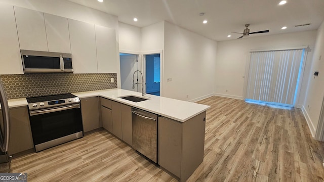 kitchen with sink, gray cabinetry, light hardwood / wood-style flooring, kitchen peninsula, and stainless steel appliances