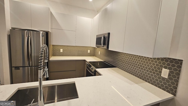 kitchen featuring light stone countertops, appliances with stainless steel finishes, white cabinets, and decorative backsplash