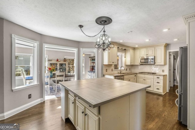 kitchen with pendant lighting, sink, stainless steel appliances, dark hardwood / wood-style floors, and cream cabinetry