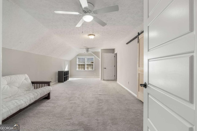 interior space with lofted ceiling, ceiling fan, a barn door, light carpet, and a textured ceiling