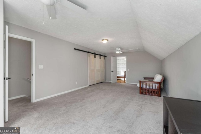 interior space featuring lofted ceiling, ceiling fan, a textured ceiling, light carpet, and a barn door