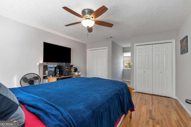 bedroom with ceiling fan, a textured ceiling, light hardwood / wood-style floors, and multiple closets