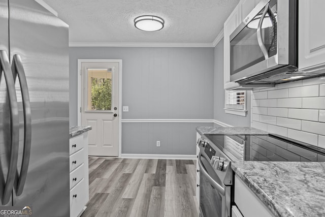 kitchen featuring light hardwood / wood-style flooring, appliances with stainless steel finishes, white cabinets, light stone countertops, and backsplash