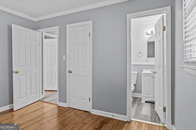 unfurnished bedroom with wood-type flooring, ornamental molding, and ensuite bathroom