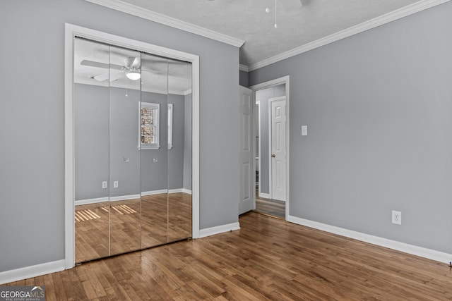 unfurnished bedroom featuring crown molding, hardwood / wood-style flooring, a closet, and ceiling fan