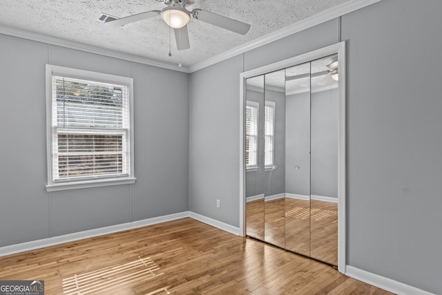 unfurnished bedroom with hardwood / wood-style flooring, ornamental molding, ceiling fan, a textured ceiling, and a closet