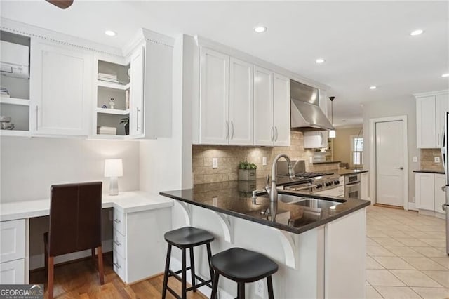 kitchen with built in desk, white cabinetry, sink, kitchen peninsula, and wall chimney exhaust hood