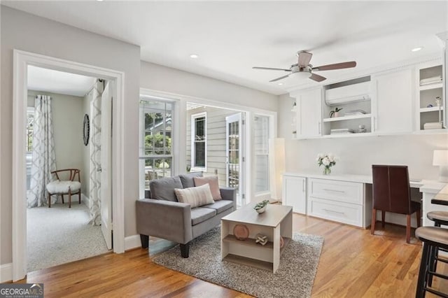 interior space with ceiling fan, built in desk, a wall unit AC, and light hardwood / wood-style flooring