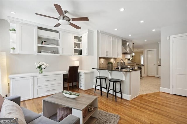 kitchen featuring a wall unit AC, built in desk, white cabinets, kitchen peninsula, and wall chimney exhaust hood