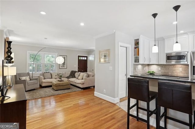 kitchen with stainless steel microwave, white cabinetry, a breakfast bar area, backsplash, and hanging light fixtures