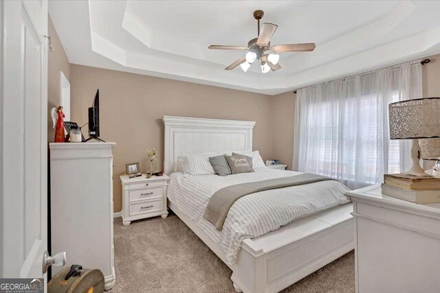 bedroom featuring light carpet, a raised ceiling, and ceiling fan