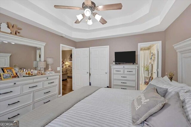 bedroom featuring ceiling fan, ensuite bathroom, a tray ceiling, and wood-type flooring