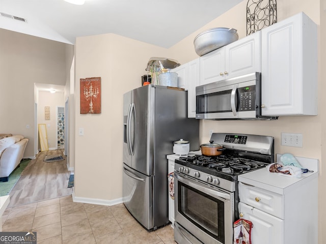 kitchen featuring stainless steel appliances, lofted ceiling, light tile patterned floors, and white cabinets